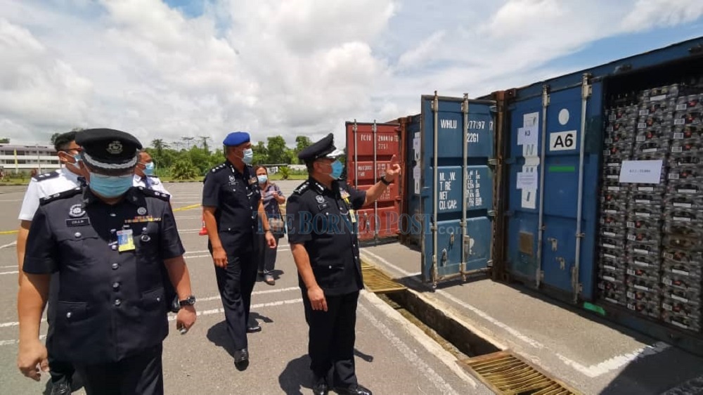 Aidi (right) inspects the contraband seized from the Tanjung Kunyit raid. At left is Collin. u00e2u20acu201d Borneo Post Online pic