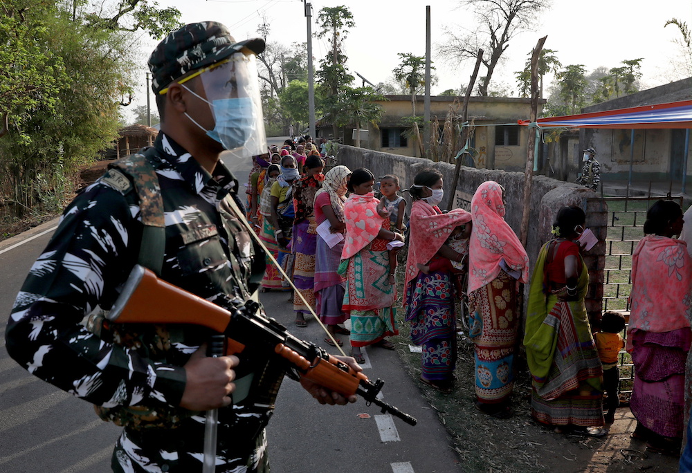 An armed policeman wearing a face shield stands guard as women wait in line to cast their votes outside a polling booth during the first phase of the West Bengal state election in Purulia district, India, March 27, 2021. u00e2u20acu201d Reuters pic