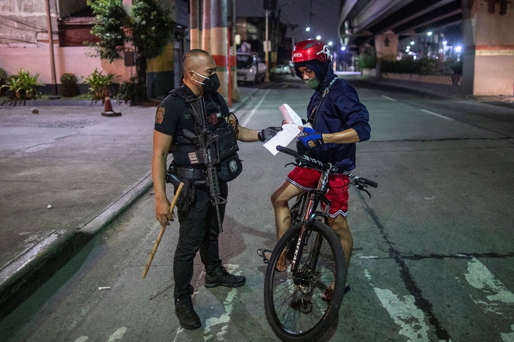 An armed police officer checks the documents of a cyclist at a checkpoint placed to implement a curfew in the country's capital amid rising Covid-19 cases, in Caloocan City, Metro Manila, Philippines March 16, 2021. u00e2u20acu2022 Reuters pic