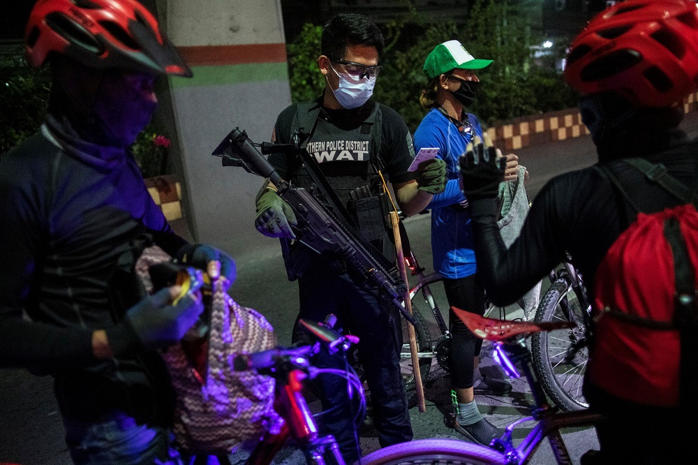 An armed police officer checks the IDs of cyclists at a checkpoint placed to implement a curfew in the country's capital amid rising Covid-19 cases, in Caloocan City, Metro Manila, Philippines March 16, 2021. u00e2u20acu2022 Reuters pic