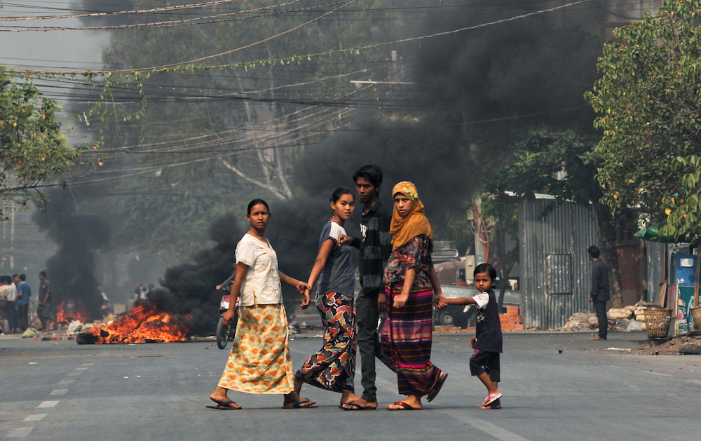 People walk on a street as barricades burn behind them during a protest against the military coup, in Mandalay, Myanmar March 27, 2021. u00e2u20acu201d Reuters picnn
