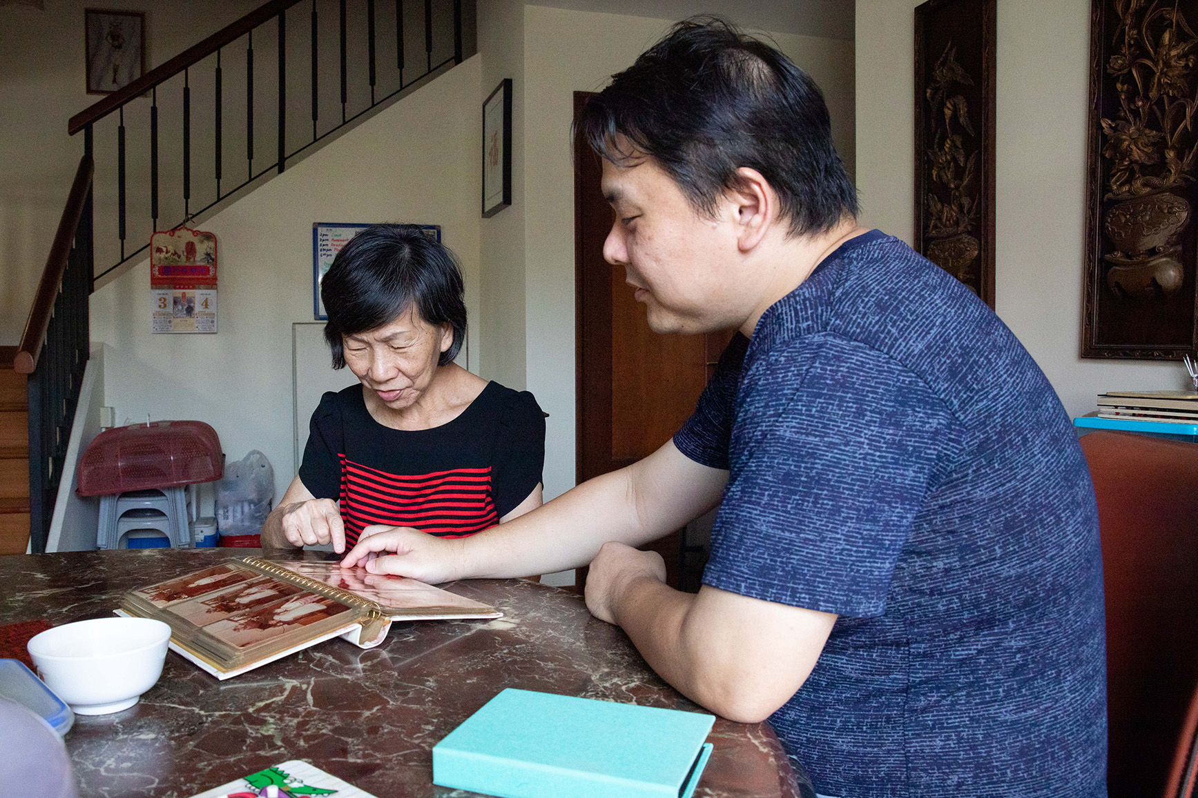 Mr Henry Koh and his 76-year-old mother who suffers from dementia, looking at old photographs in their home on March 3, 2021. — Photo by Ili Nadhirah Mansor for TODAY