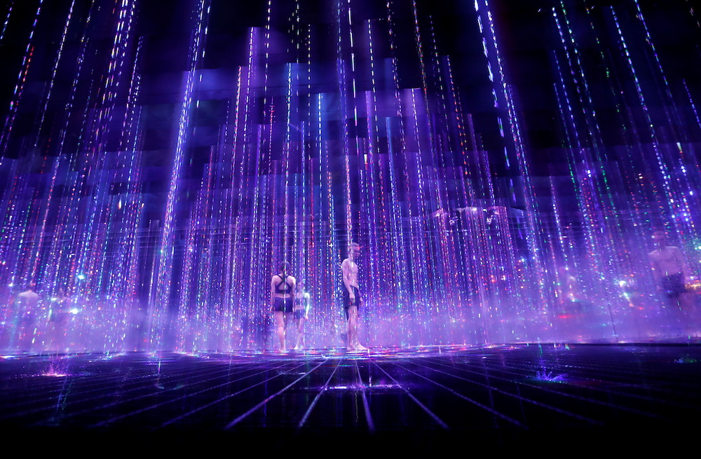 Staffs of teamLab wearing swimming suits walk inside digital artwork combined with light, water and sound during a demonstration of TikTok teamLab Reconnect, digital artwork combined with sauna, ahead of its opening to the public this month in Tokyo, Japa
