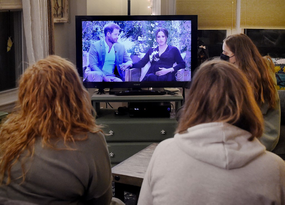This photo illustration shows people wearing face masks, watch a televised conversation between Britainu00e2u20acu2122s Prince Harry with his wife Meghan Markle and US host Oprah Winfrey, in Arlington, Virginia March 7, 2021. u00e2u20acu201d AFP pic