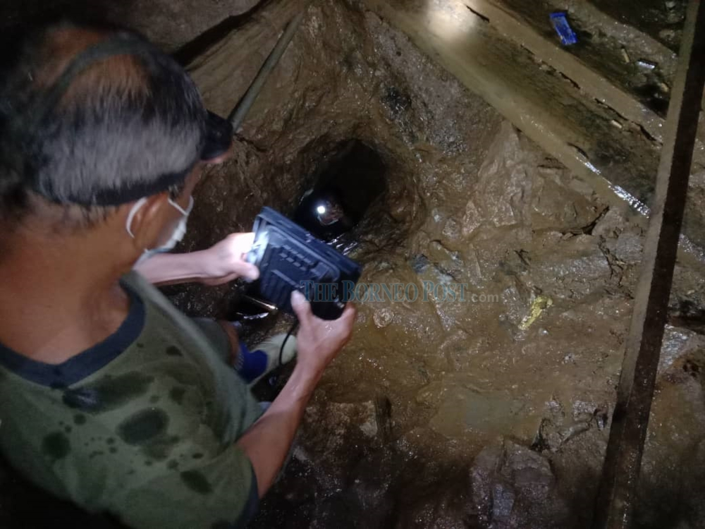 A member of the rescue effort shines a light into the hole where a hand can be seen holding up a lit torchlight. — Borneo Post Online pic