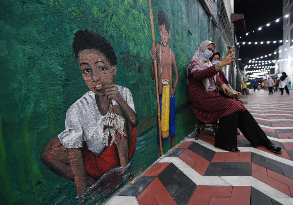 Kuantan residents pose for a picture against the background of a mural painting of the life of the Orang Asli community at Kuantan Art Street, March 2, 2021. u00e2u20acu201d Bernama pic 