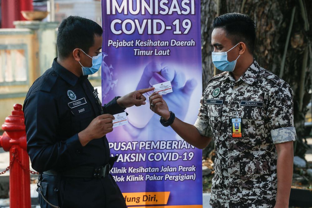 A Prisons Department personnel and a policeman hold up their vaccination cards after receiving their Covid-19 jabs at the Jalan Perak Health Clinic in Jelutong March 4, 2021. u00e2u20acu201d Picture by Sayuti Zainudin