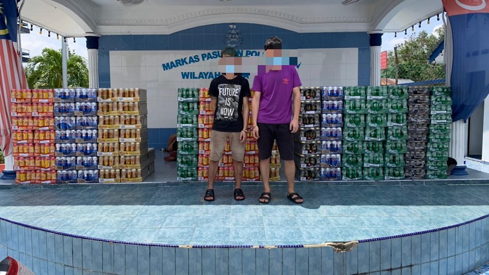 The two suspects with the untaxed alcoholic beverages and liquor at the Region Two Marine Police Force headquarters in Tampoi, Johor Baru. u00e2u20acu201d Picture courtesy of Region Two Marine Police Force