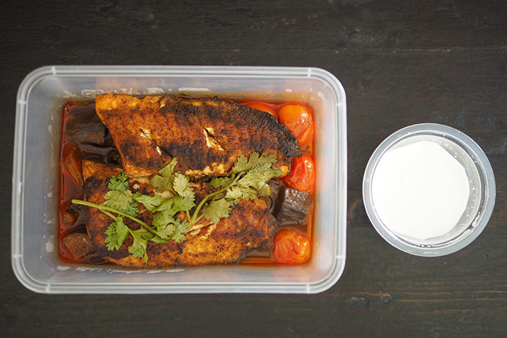 The fish is packed neatly with the eggplant and tomatoes underneath