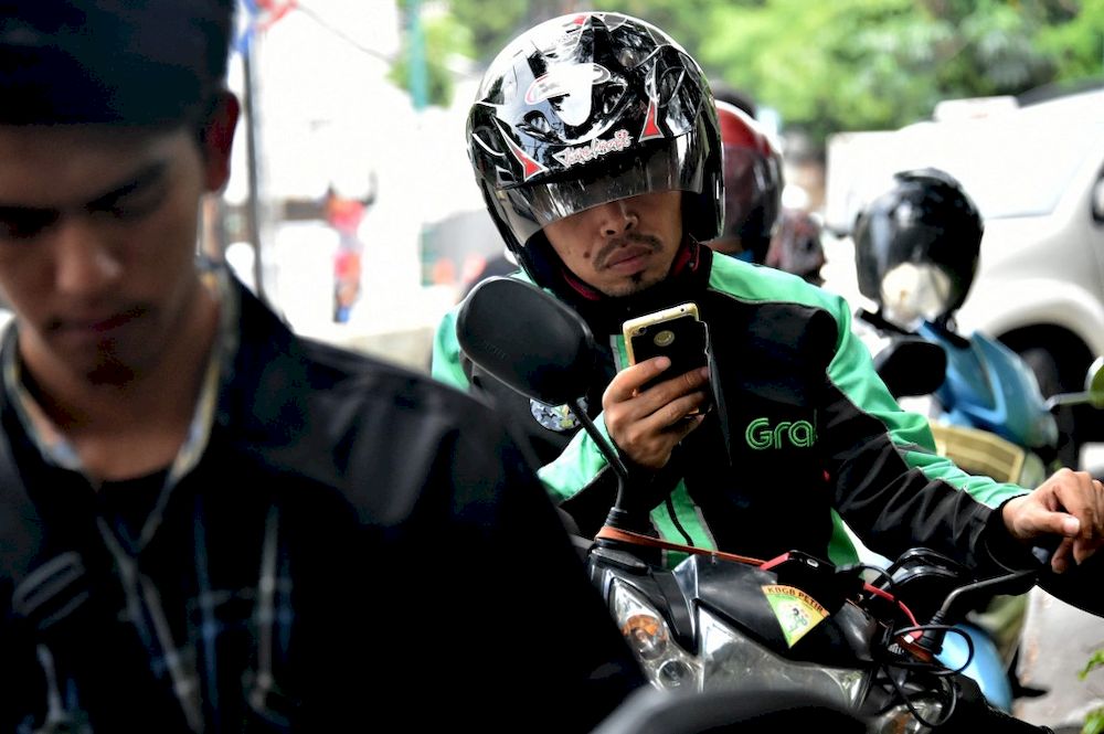 In this file photograph taken on February 2, 2017, a u00e2u20acu02dcGrabBikeu00e2u20acu2122 motorcyclist uses his mobile phone in Jakarta. Ride-hailing company Grab plans a US listing after merging with the investment fund Altimeter Capital Management. u00e2u20acu201d AFP pic