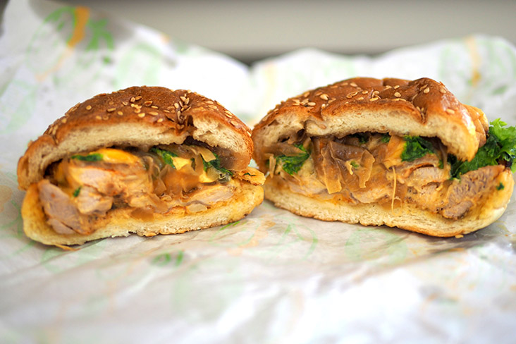 A cross section of the Cajun grilled chicken burger that has caramelised onions and vegetables with a soft brioche bun