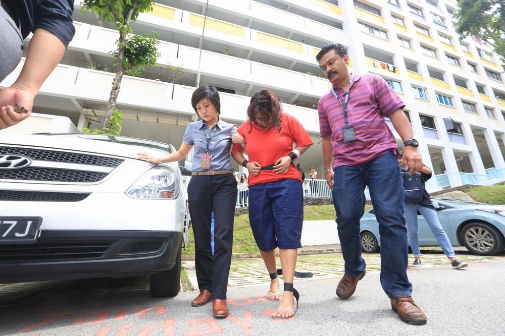 Gaiyathiri Murugayan (centre) being led by investigators to her Bishan flat in 2016 for a re-enactment of how her domestic worker died. u00e2u20acu201d TODAY pic