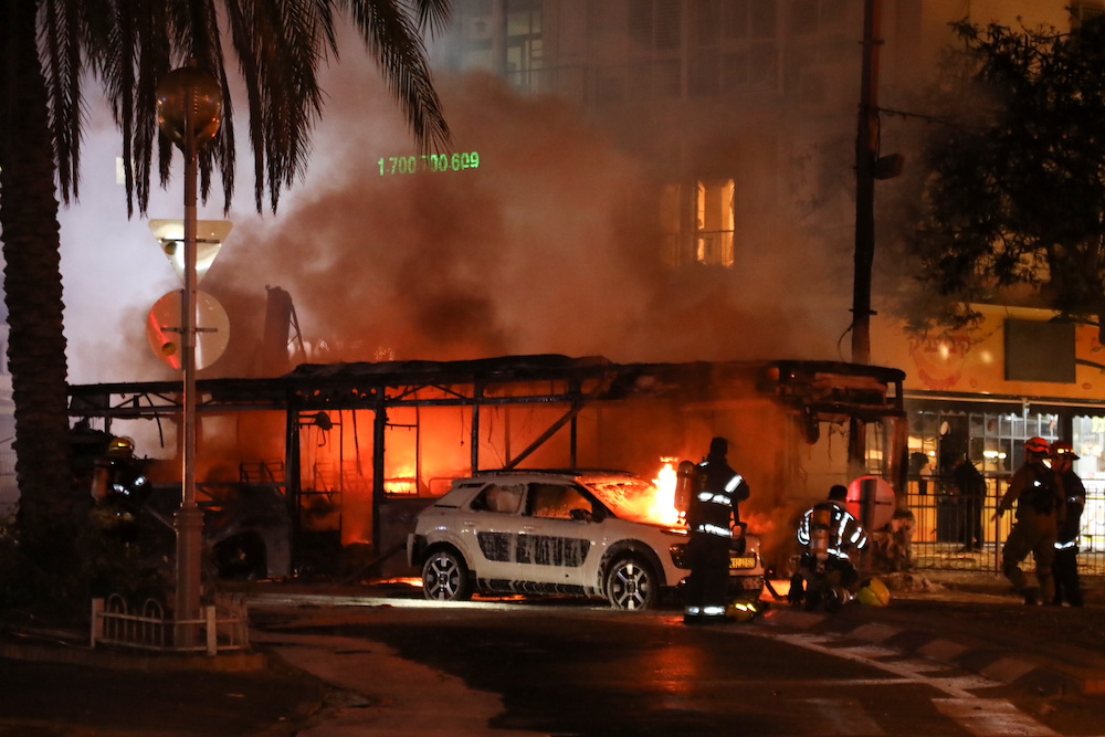 Israeli firefighters, security and rescue forces stand next to a burning bus and car that were hit by a rocket fired from Gaza towards Holon, Israel May 11, 2021. u00e2u20acu201d Reuters/Gidon Markovitz pic