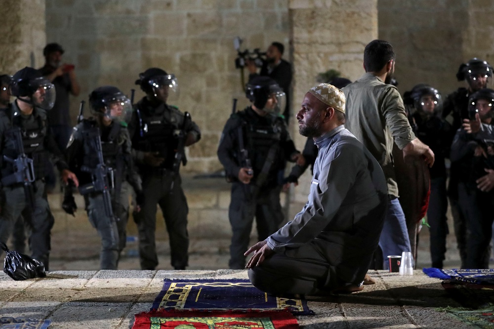 A Palestinian man prays as Israeli police gather during clashes at the compound that houses Al-Aqsa Mosque in Jerusalemu00e2u20acu2122s Old City May 7, 2021. u00e2u20acu201d Reuters pic