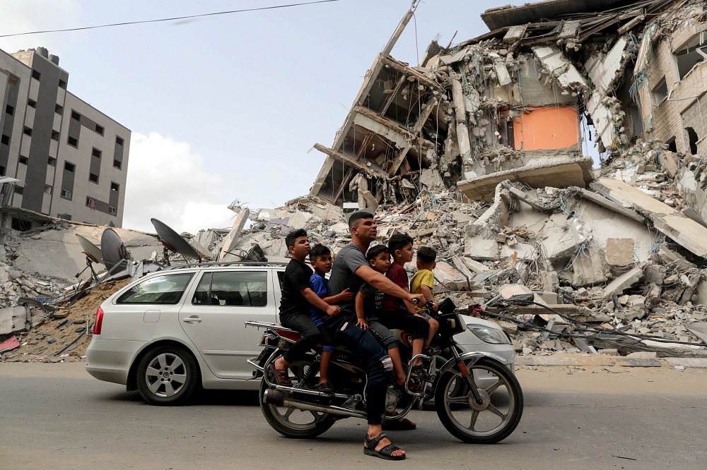 Palestinians ride a motorcycle past the site of an Israeli air strike, after Israel- Hamas truce, in Gaza May 21, 2021. — Reuters pic