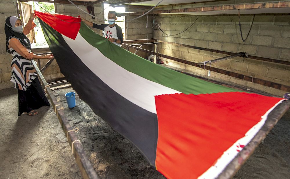 Batik entrepreneur Yuslinawati Othman (left) with her cousin Wan Hafizul Wan Johari, showing the Palestinian flag that has been dyed, at her house in Kampung Baru Salor, Kota Baru, May 24, 2021. u00e2u20acu201d Bernama pic