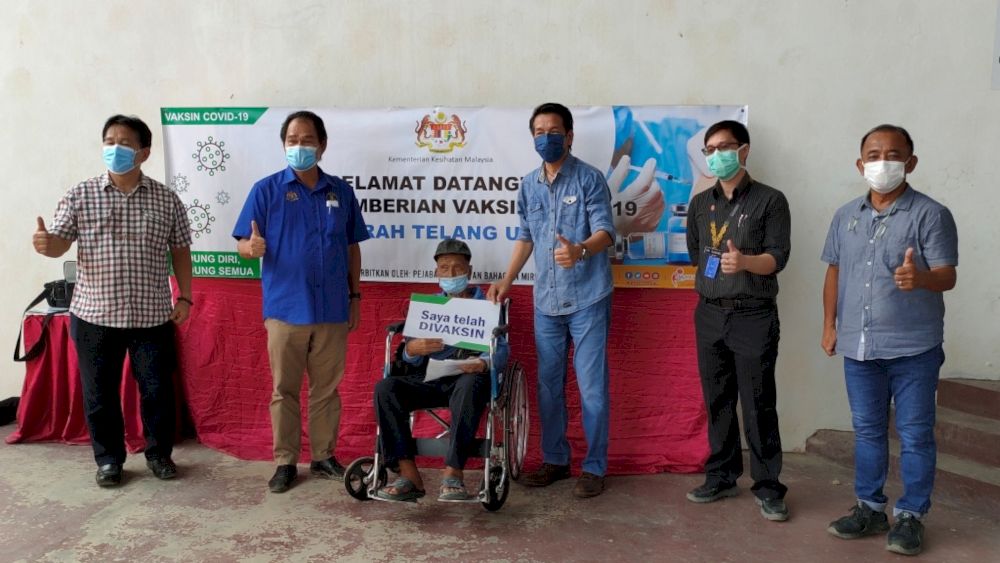 Dennis (third right) and Anyi (second left) join others in a group photo at the hall of SJKC Kee Teein Long Lama, which serves as the vaccination centre for the district. u00e2u20acu201d Borneo Post pic