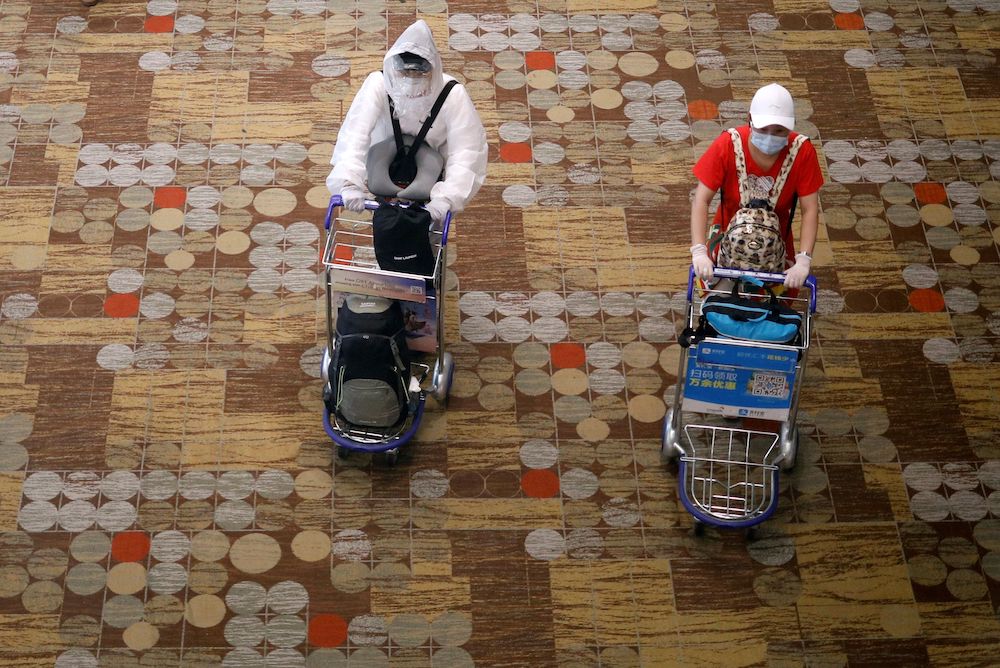 A person wearing a protective gear walks next to a person wearing a face mask and gloves at Singaporeu00e2u20acu2122s Changi Airport, following the outbreak of the coronavirus disease March 30, 2020. u00e2u20acu201d Reuters picnnnn