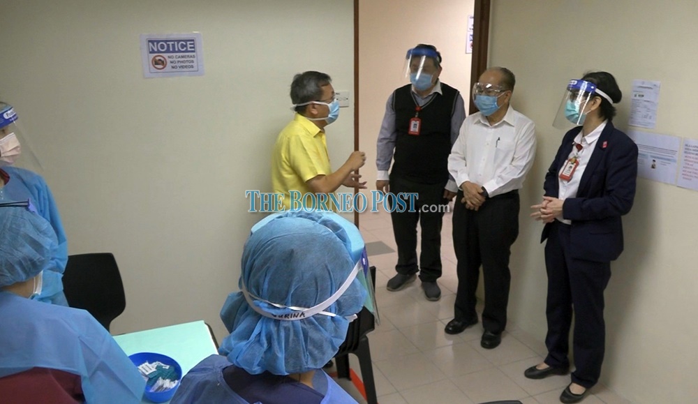Uggah (second right), Dr Sim (fourth right) and Lau (third right) in a serious discussion as they visit the space where the vaccination is carried out. u00e2u20acu2022 Borneo Post pic