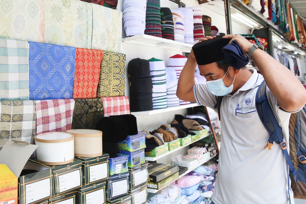 A man tries on a songkok at Jalan Masjid India on the eve of Hari Raya Aidilfitri May 12, 2021. — Picture by Choo Choy May