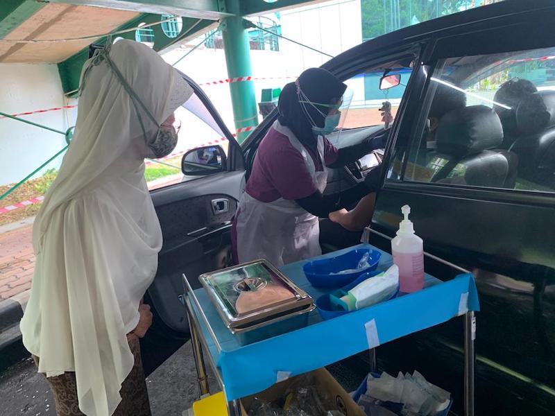 Fatimah (left) looks on as a health frontliner administers vaccine on an OKU recipient at the drive-thru vaccination station in Normah Medical Specialists Centre in Kuching. u00e2u20acu201d Borneo Post pic