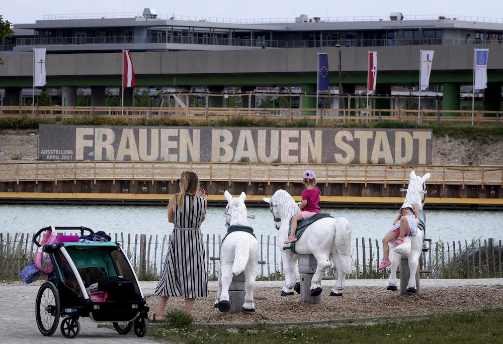 Children play in a playground facing large panels proclaiming the slogan ‘Women build the city’ next to some of the building sites that will eventually contain 12,000 new housing units, at Vienna's suburb Seestadt, Austria, on June 8, 2021. — AFP pi