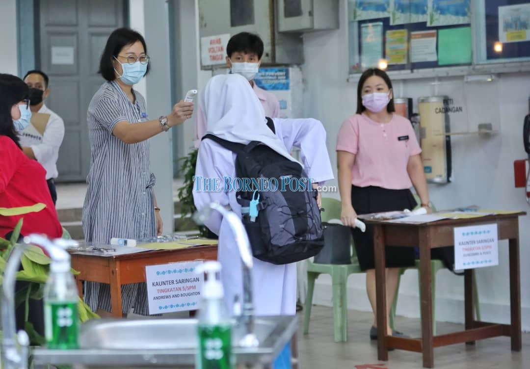 A teacher checking the body temperature of a student. u00e2u20acu2022 Borneo Post pic