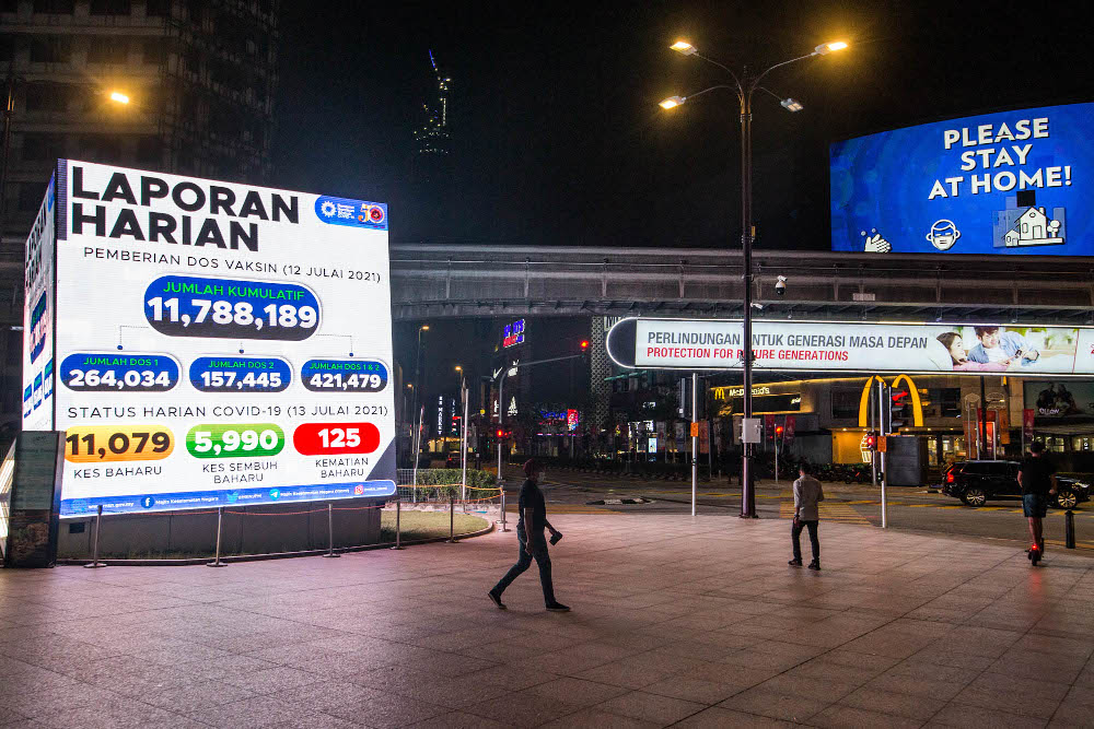 Pedestrians walk past a digital screen displaying the new daily record of Covid-19 cases in Kuala Lumpur July 13, 2021. u00e2u20acu201d Picture by Firdaus Latif