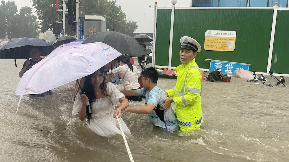 A traffic police officer guides residents to cross a flooded road with a rope during heavy rainfall in Zhengzhou, Henan province, China July 20, 2021. u00e2u20acu201d Reuters picnn