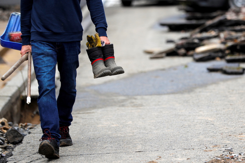 A man carrying boots and cleaning equipment walks through a damaged road following heavy rainfall in Dinant, Belgium July 25, 2021. u00e2u20acu201d Reuters pic