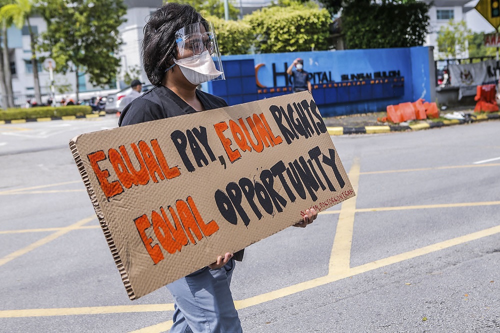 A contract doctor holds aloft a placard demanding equal treatment during a strike at the Sungai Buloh Hospital July 26, 2021. — Picture by Hari Anggara 