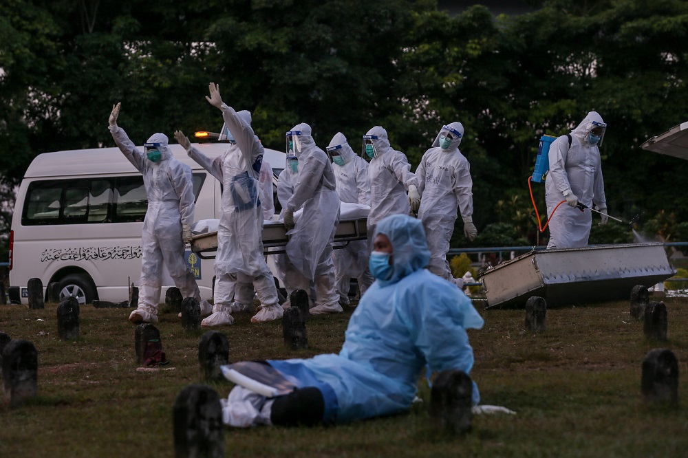 A Civil Defence Force member rests while his colleagues in the background continue with the burial tasks even as the sun sets.