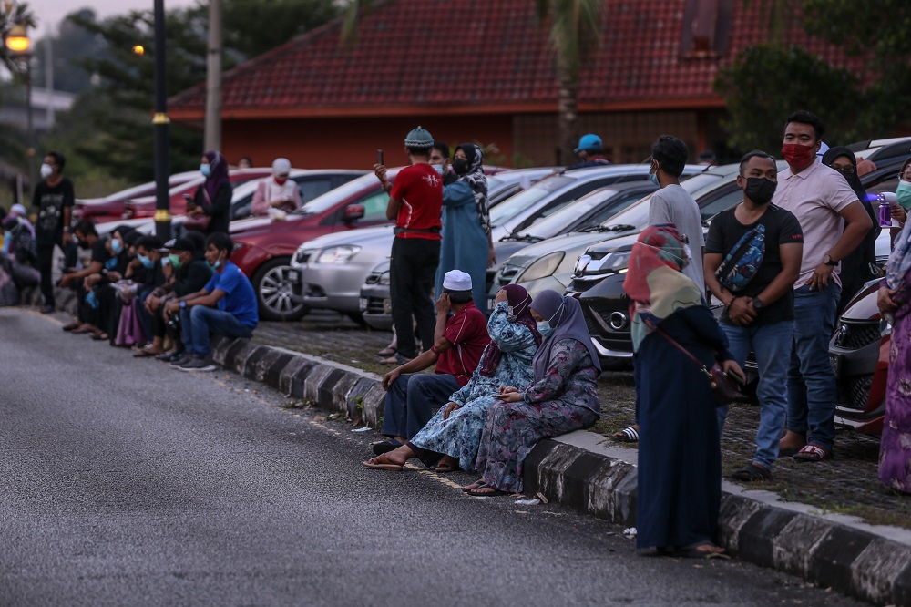 Family members wait in the distance as their loved ones are buried at the Raudhatul Sakinah Bukit Kiara 1 Muslim cemetery. — Picture by Ahmad Zamzahuri