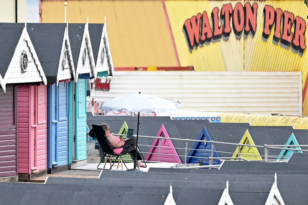 A woman works on a laptop as she sits under an umbrella outside a beach hut at Walton-on-the-Naze, in south-east England on July 15, 2021. u00e2u20acu201d AFP pic