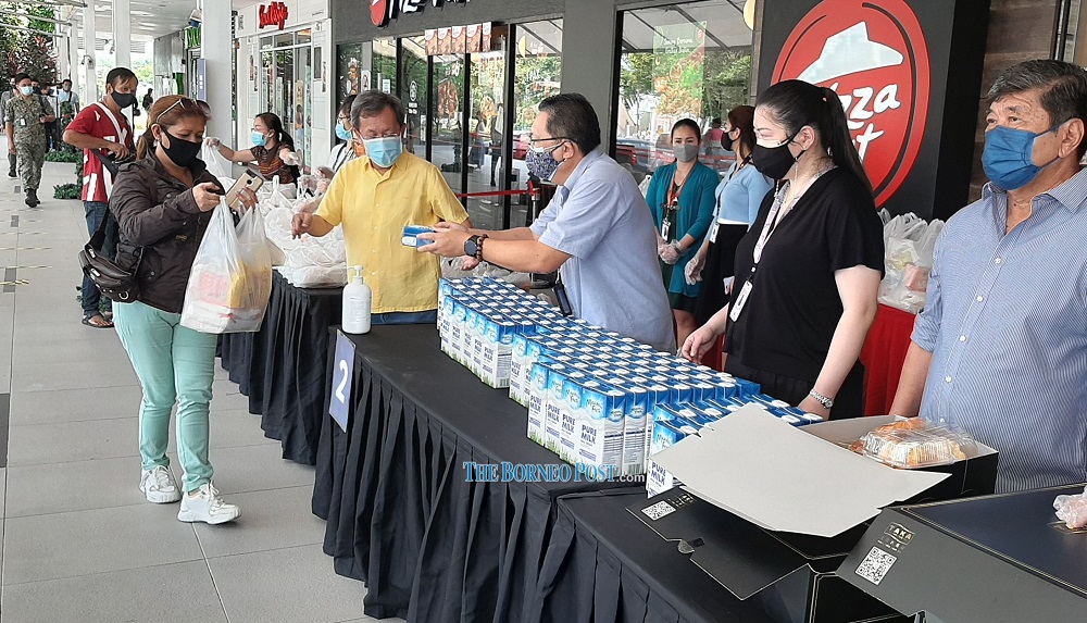 Dr Sim (fourth right) and Wee (third right) hand over a food pack to a recipient. From right are James and Lisa. u00e2u20acu201d Borneo Post Online pic