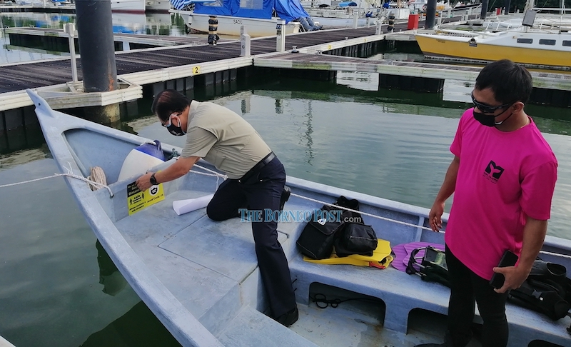 Lee (left) is seen sticking a physical distancing reminder sticker on a diving boat, before flagging off the first batch of divers. u00e2u20acu201d Borneo Post pic