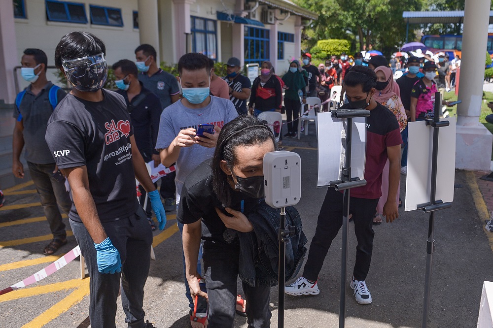 Foreign workers check their temperatures before entering the Komplek Sukan PKNS in Kelana Jaya to receive their Covid-19 vaccination shot August 10, 2021. u00e2u20acu201d Picture by Miera Zulyana