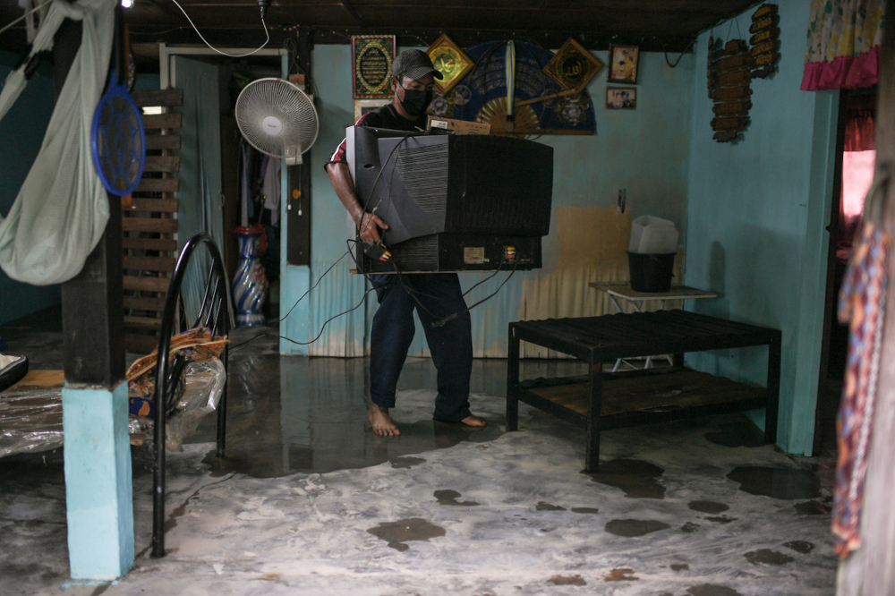 Roslan Mat Isa, 52, carries a television after his house was inundated with floodwater in Kampung Masjid, Balik Pulau, August 19, 2021. u00e2u20acu201d Bernama pic 