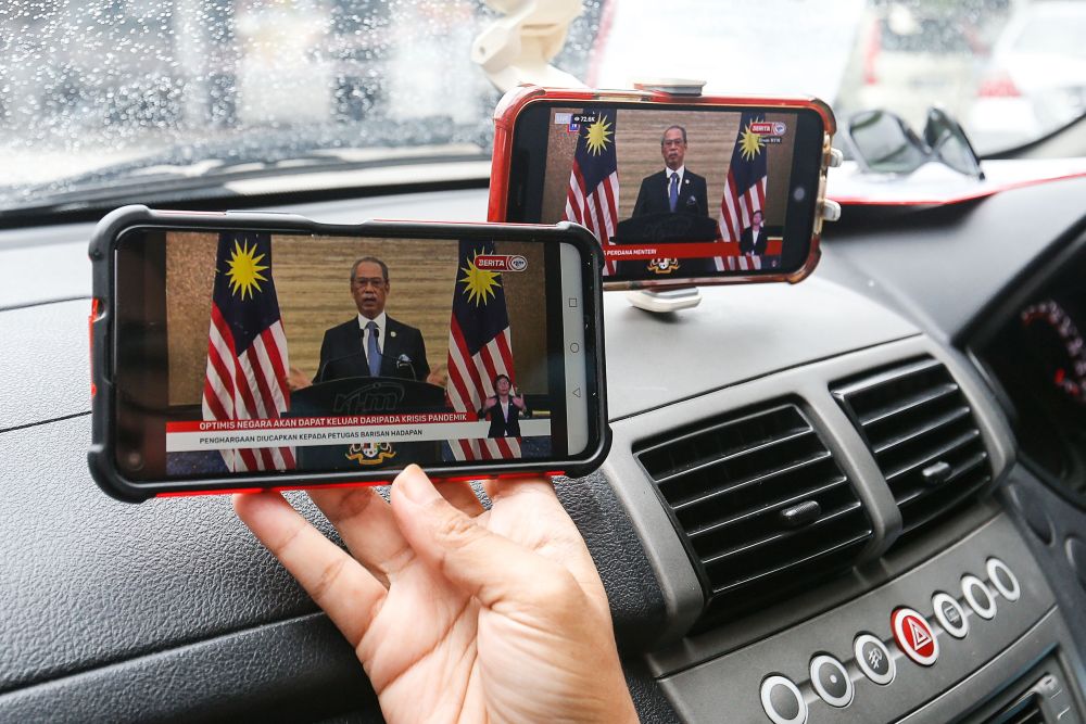 A woman watches a live telecast of caretaker Prime Minister Tan Sri Muhyiddin Yassinu00e2u20acu2122s speech on her phone in Bayan Baru August 16, 2021. u00e2u20acu201d Picture by Sayuti Zainudin