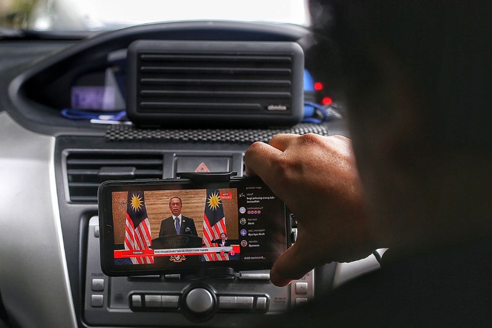 A man watches a live telecast of caretaker Prime Minister Tan Sri Muhyiddin Yassin's speech on his phone August 16, 2021. — Picture by Ahmad Zamzahuri
