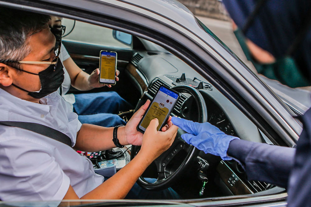 A man and his passenger show the Covid-19 digital vaccination certificate to police at the Plaza Bentong roadblock, August 11, 2021. u00e2u20acu2022 Picture by Hari Anggara 