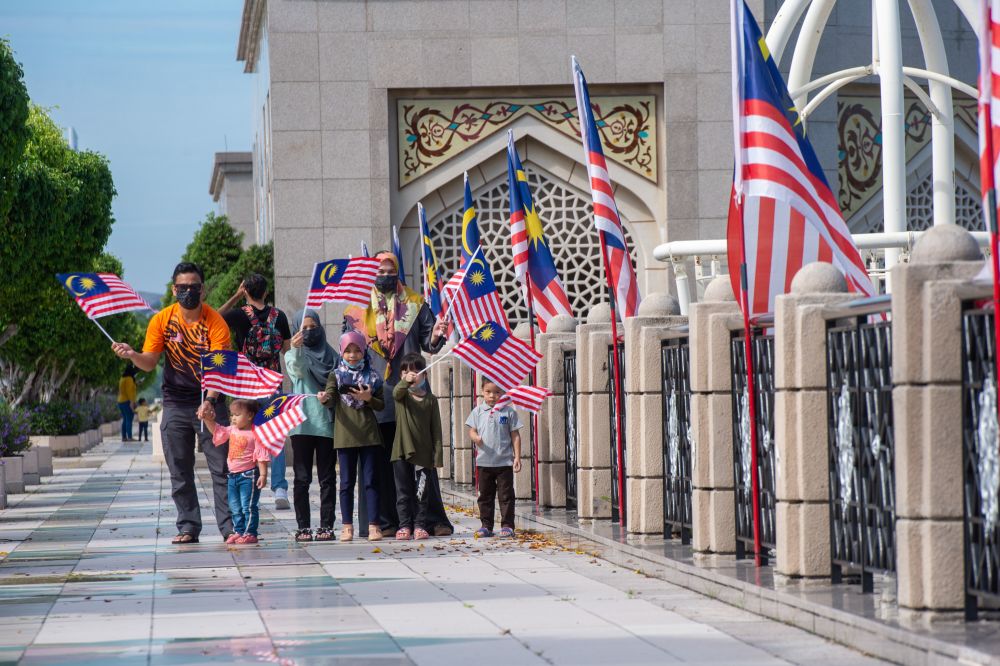 A man and his family are seen waving Malaysian flags on National Day in Dataran Gemilang, Putrajaya August 31, 2021. — Picture by Shazwan Zaidon