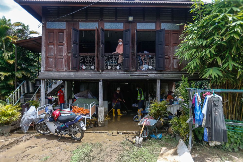 Ku Masturah looks on as family members help with cleaning up work at home following flash floods in Yan August 25, 2021. — Picture by Sayuti Zainudin