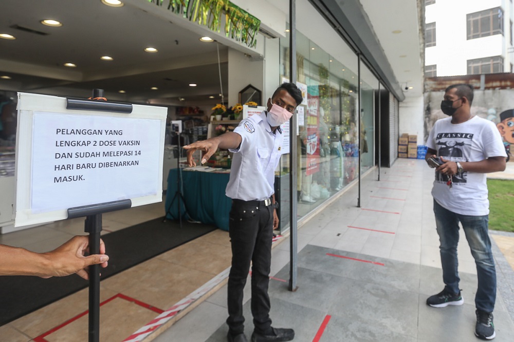 A security personnel points at a notice informing customers of Covid-19 vaccination requirements at a shop in Kuala Lumpur August 17, 2021. u00e2u20acu201d Picture by Yusof Mat Isa