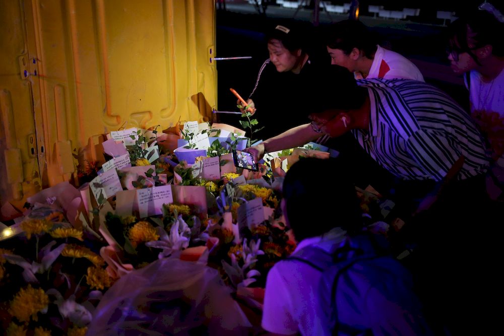 People hold their mobile phones in front of flowers placed near an entrance to a subway station of Metro Line 5 in memory of flood victims following heavy rainfall in Zhengzhou, Henan province, China July 26, 2021. u00e2u20acu201d China Daily pic via Reuters