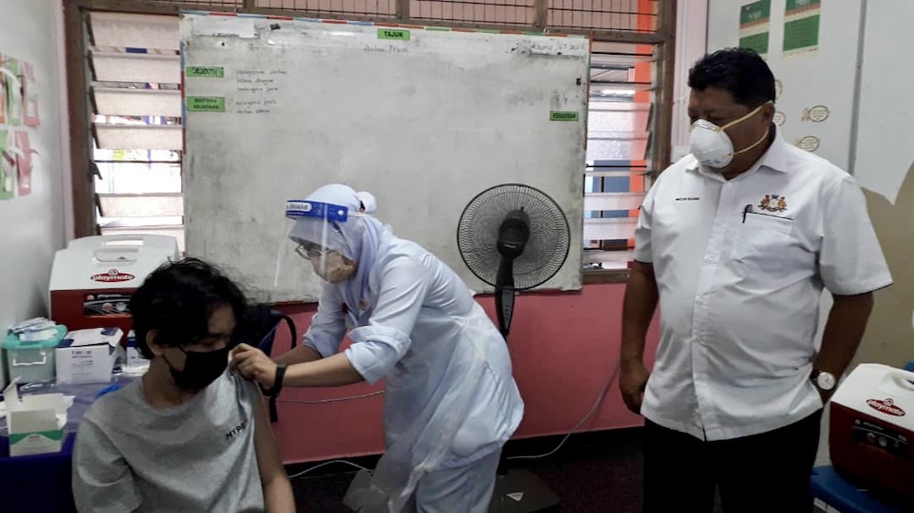 Johor Education, Information, Heritage and Culture Committee chairman Mazlan Bujang (far right) observes the vaccination of a student during his visit to Sekolah Menengah Kebangsaan (SMK) Taman Daya in Johor Baru September 20, 2021 u00e2u20acu201d Picture by Ben Tan