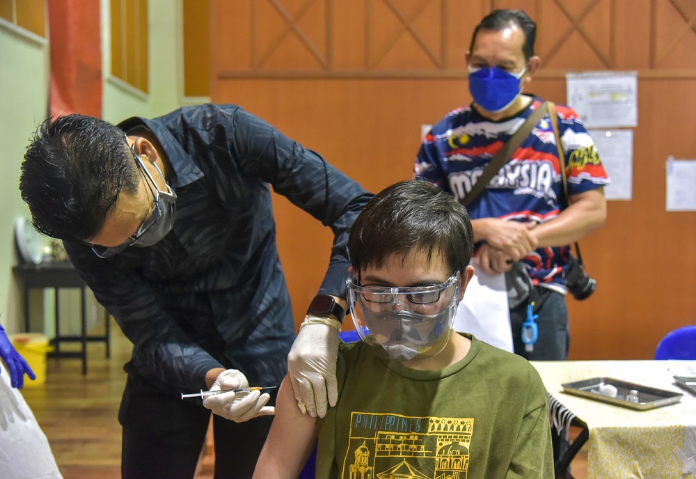 Labuan Health Department director Dr Ismuni Bohari administers the Covid-19 vaccine to Nuqman Zaidan Ramlen, 17 at Dewan Kompleks Darul Kifayah MAIWP in Labuan September 11, 2021. u00e2u20acu2022 Bernama pic