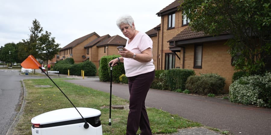 Sheila, 71, accepts a delivery through the app from an autonomous robot called Starship delivering groceries from a nearby Co-op supermarket in Milton Keynes, England. u00e2u20acu201d ETX Studio pic