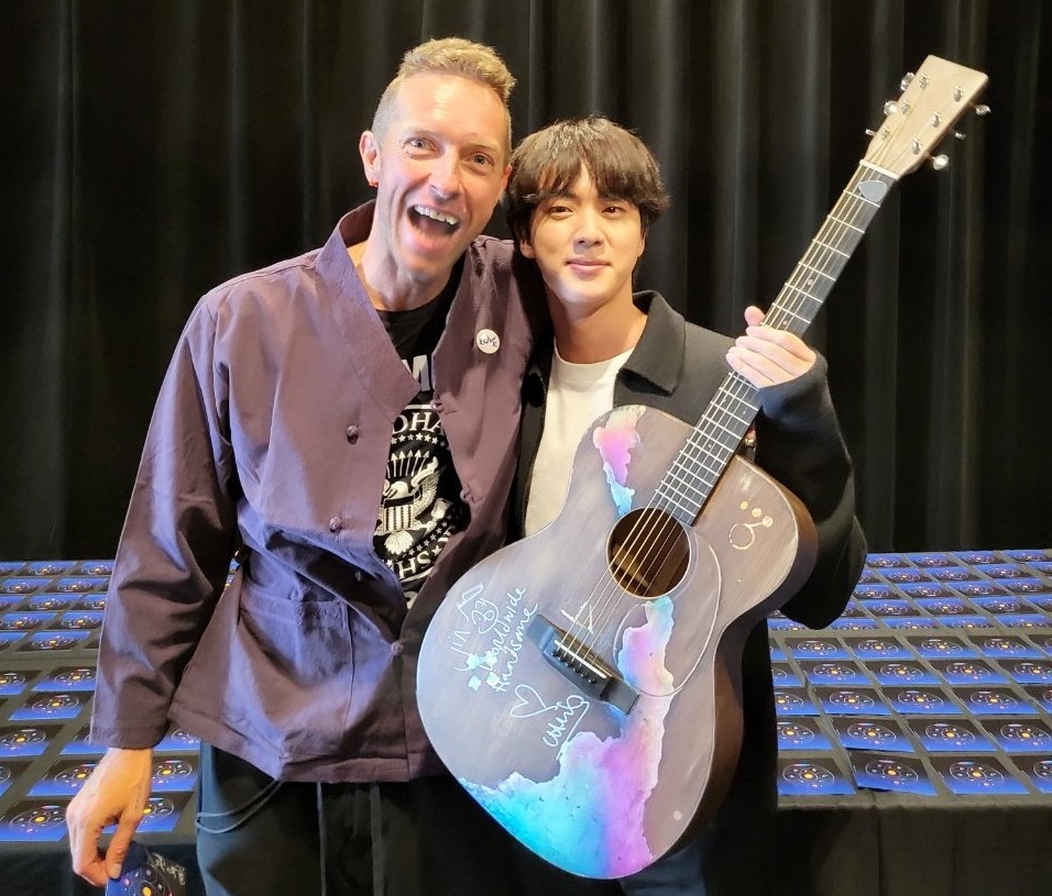 Jin (right) holding the guitar given to him by Chris Martin. u00e2u20acu201d Picture via Twitter