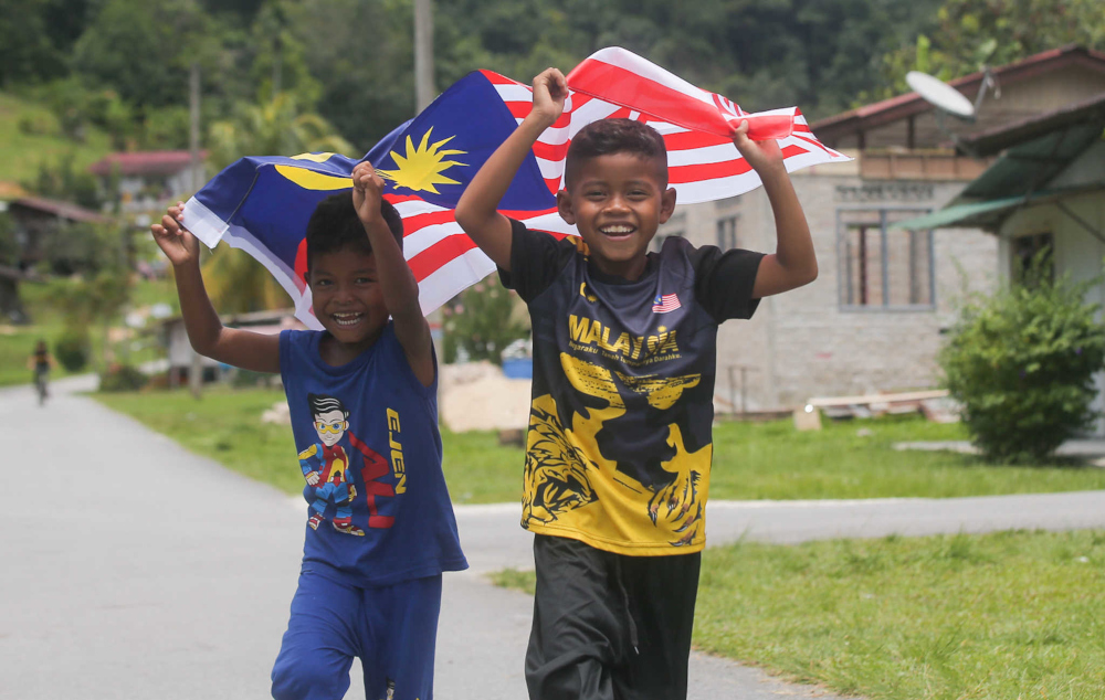 Children from Kampung Orang Asli Chadak, Ulu Kinta in Perak run with the Jalur Gemilang September 15, 2021. — Picture by Farhan Najib